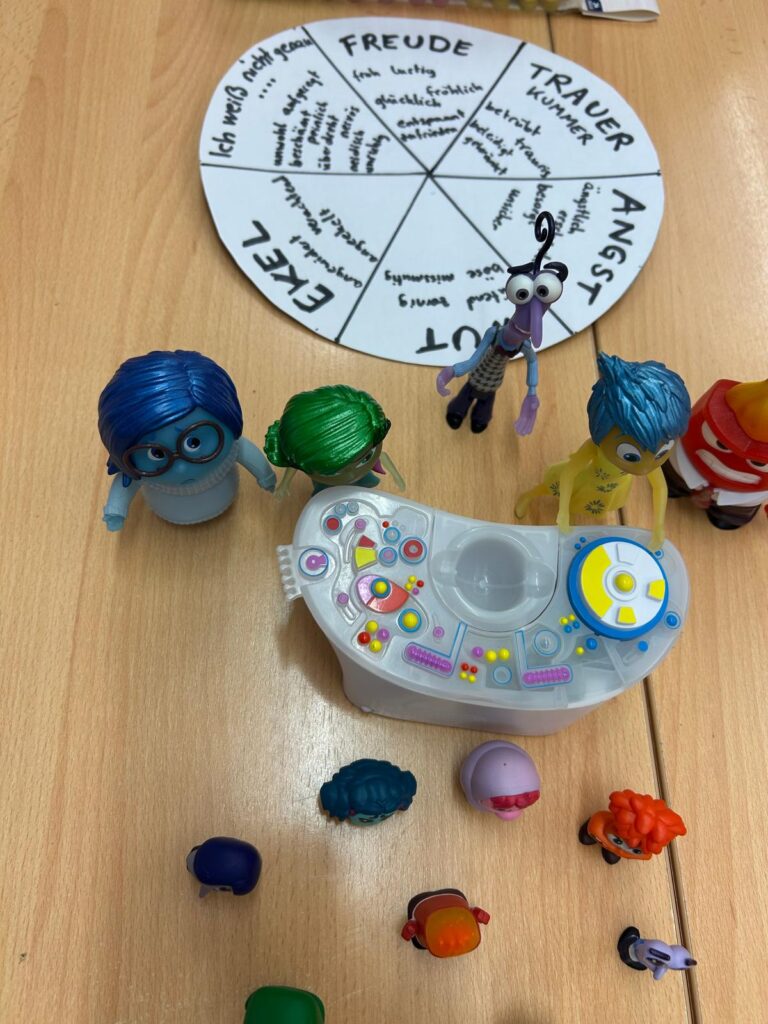 Kleine Spielfiguren auf einem Tisch mit Text auf Papier zum Thema Emotionen